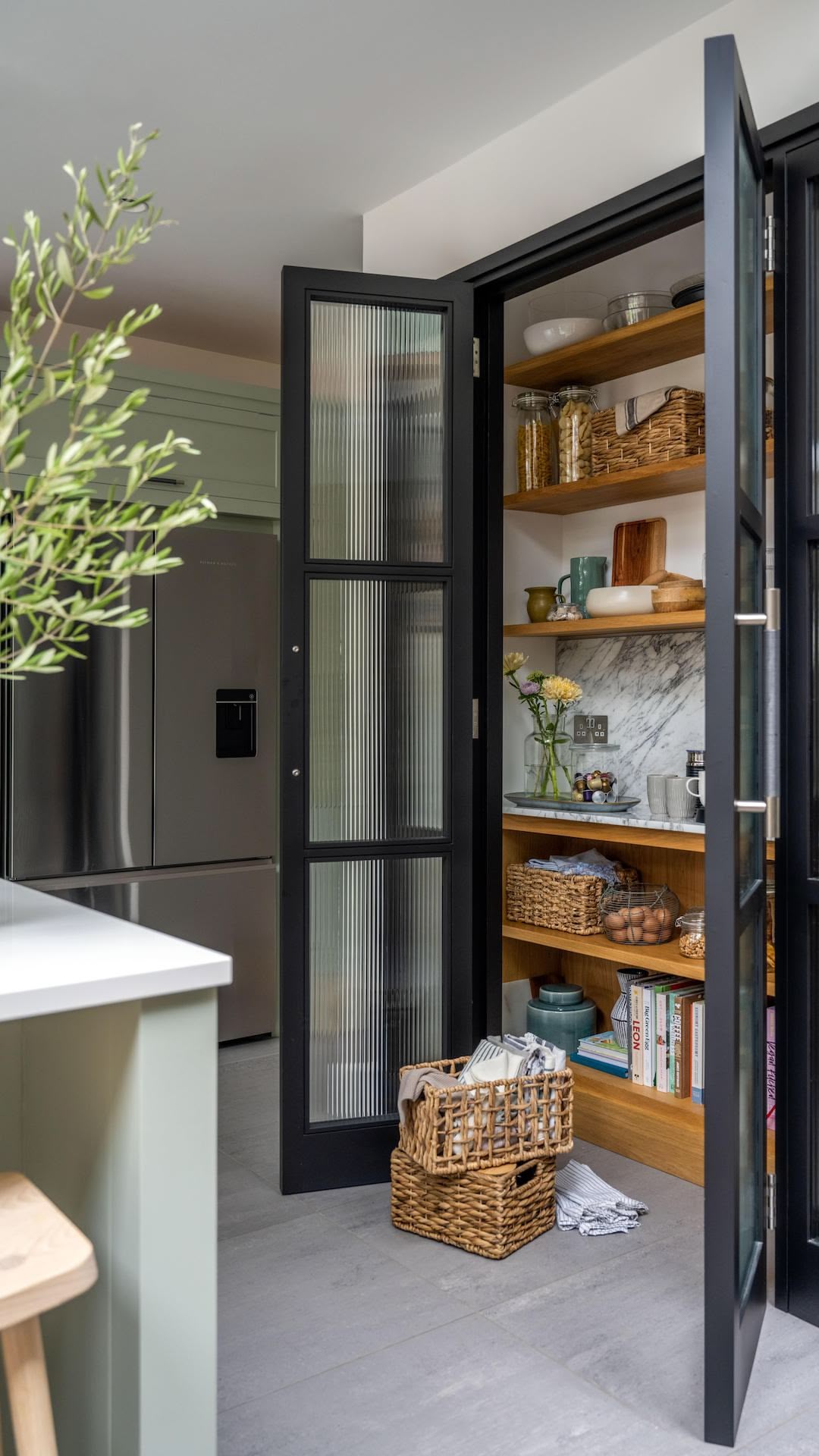Black framed kitchen pantry with glass doors open to show organised storage and shelving