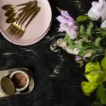 Closeup of black marble worktop with pink crockery and gold cutlery