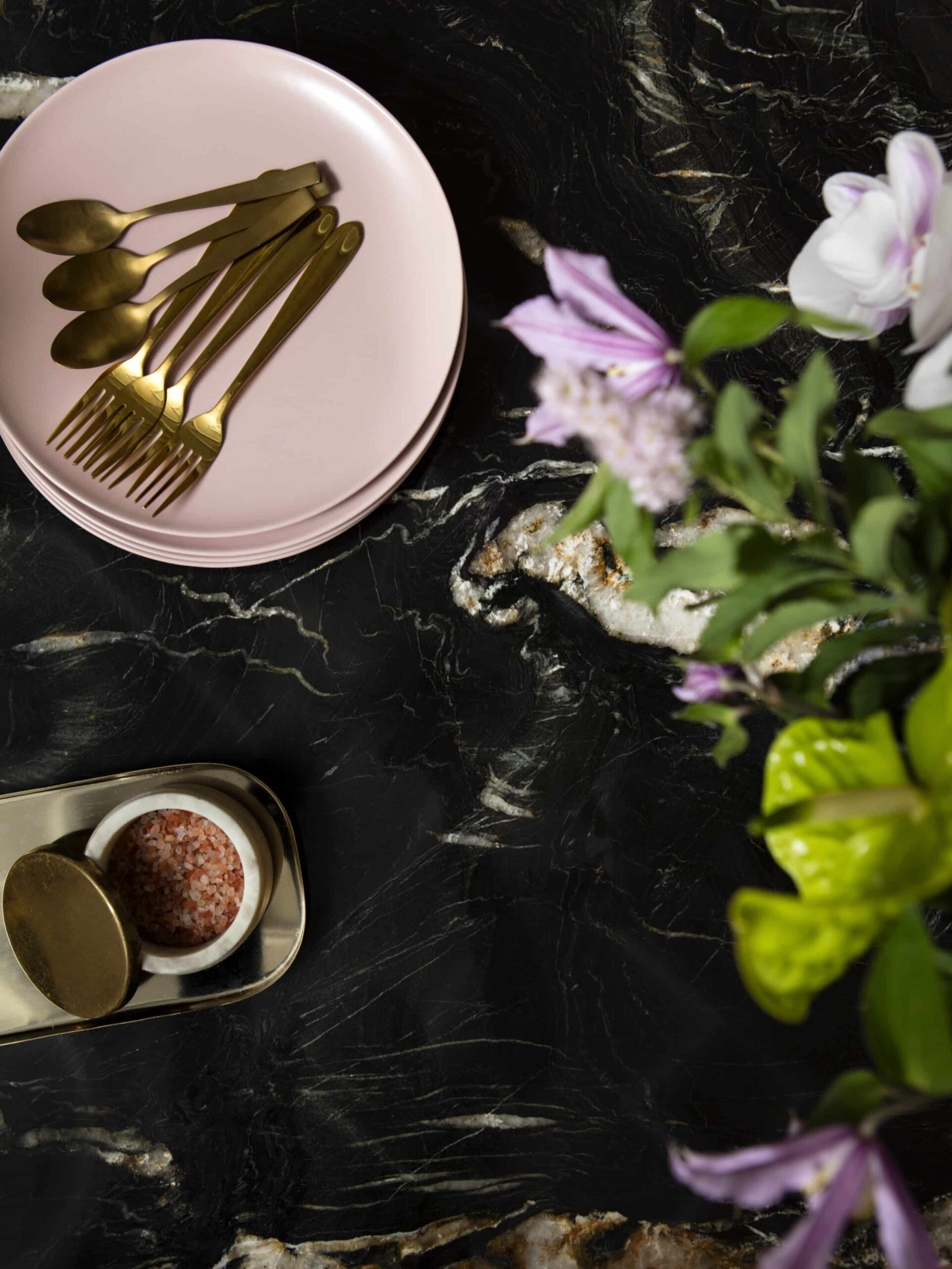 Closeup of black marble worktop with pink crockery and gold cutlery