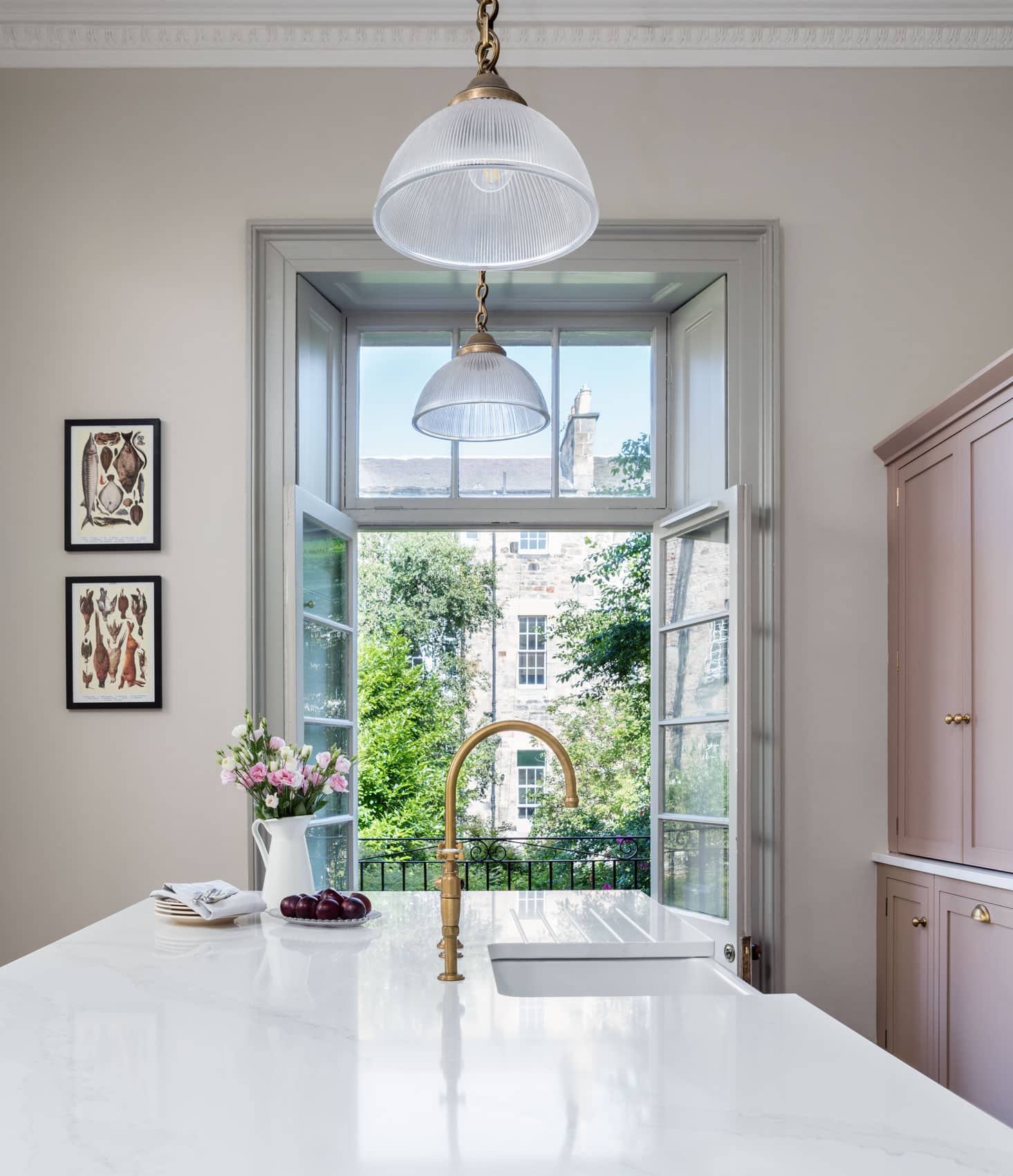 White marble kitchen island worktop with basin sink and gold tap in front of open French windows