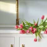 Closeup of white sink with gold tap and white kitchen cabinetry with gold handles
