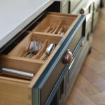 Vibrant green kitchen cupboard with brass handle open to reveal oak cutlery dividers