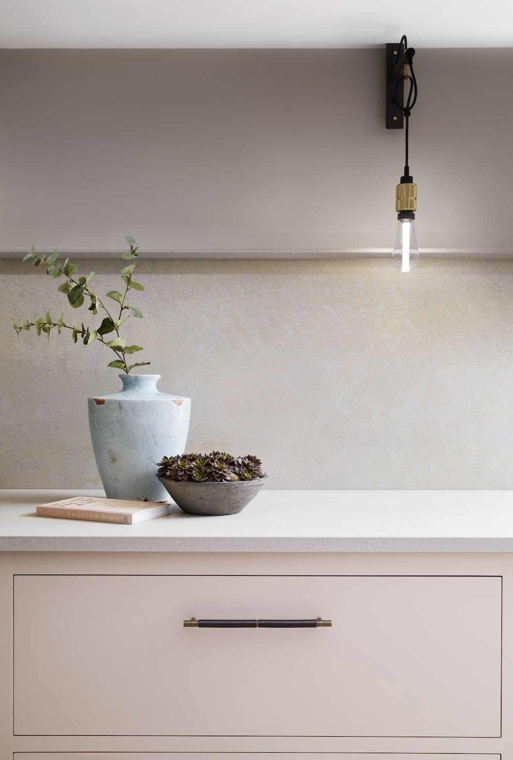 Soft pink Linear kitchen cabinetry with dark brown handles and white worktop