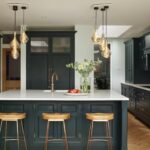 Vibrant green kitchen island with white worktop, integrated sink with brass tap and oak bar stools
