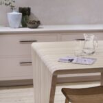 Natural wooden table with stool in front of soft pink cabinetry with white worktop