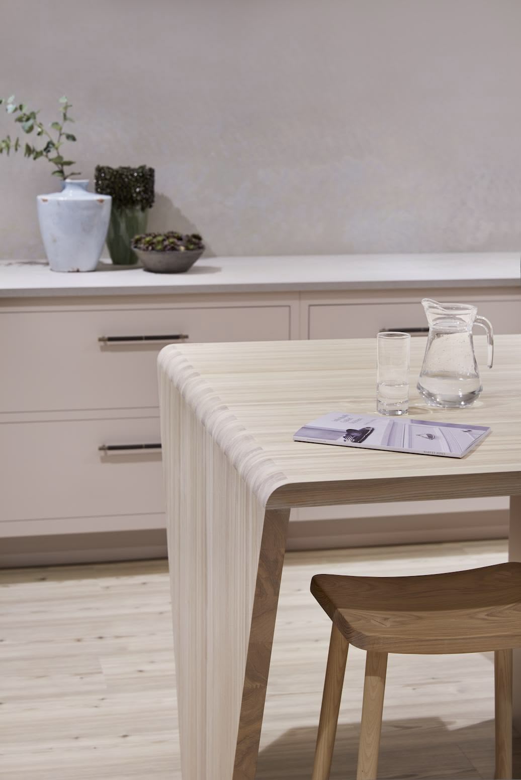 Natural wooden table with stool in front of soft pink cabinetry with white worktop