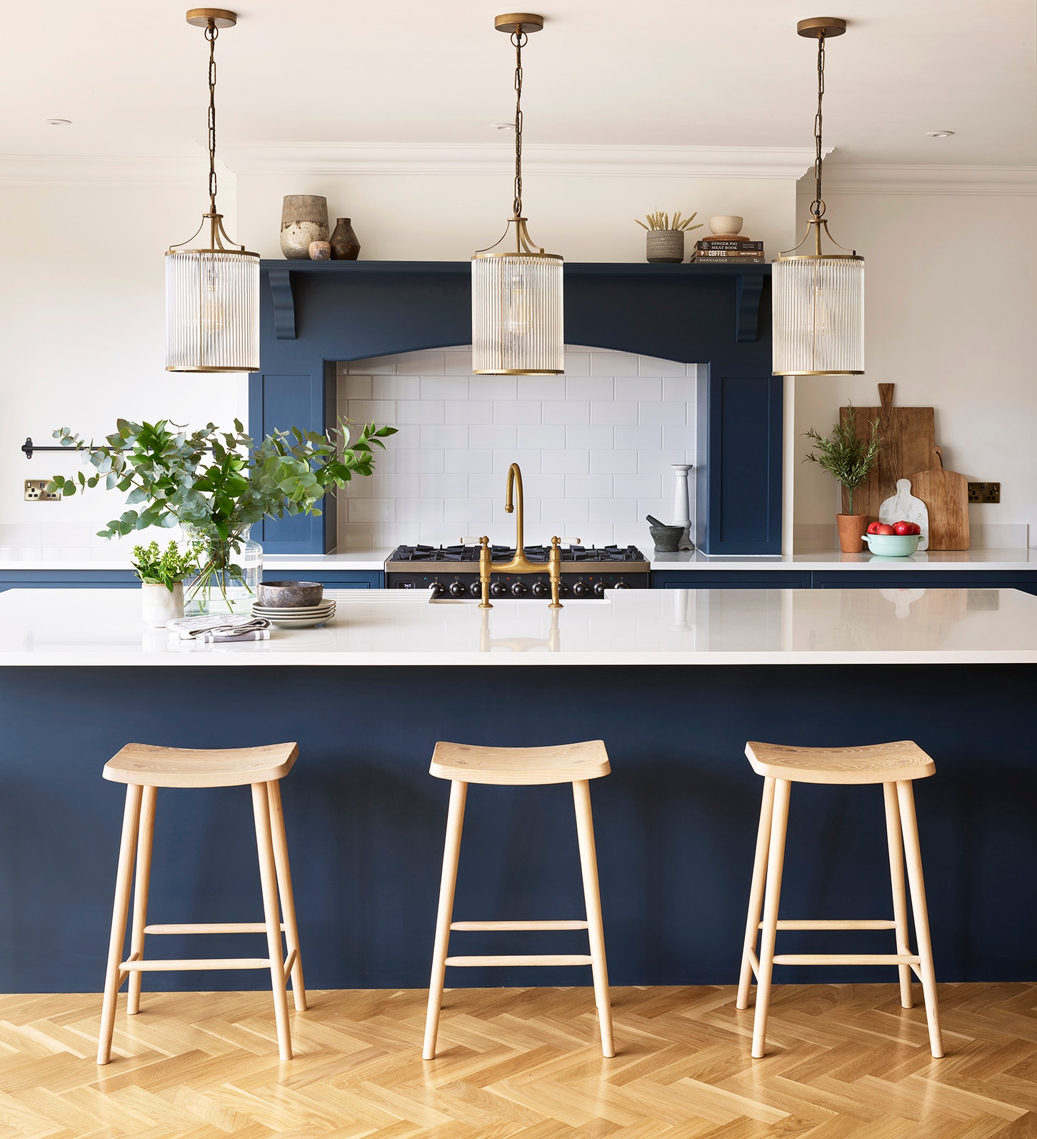 Deep blue kitchen island with white worktop featuring wooden stools