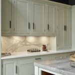 Pale green Arbor kitchen cabinetry with white work tops and kitchen island featuring a grey marble worktop