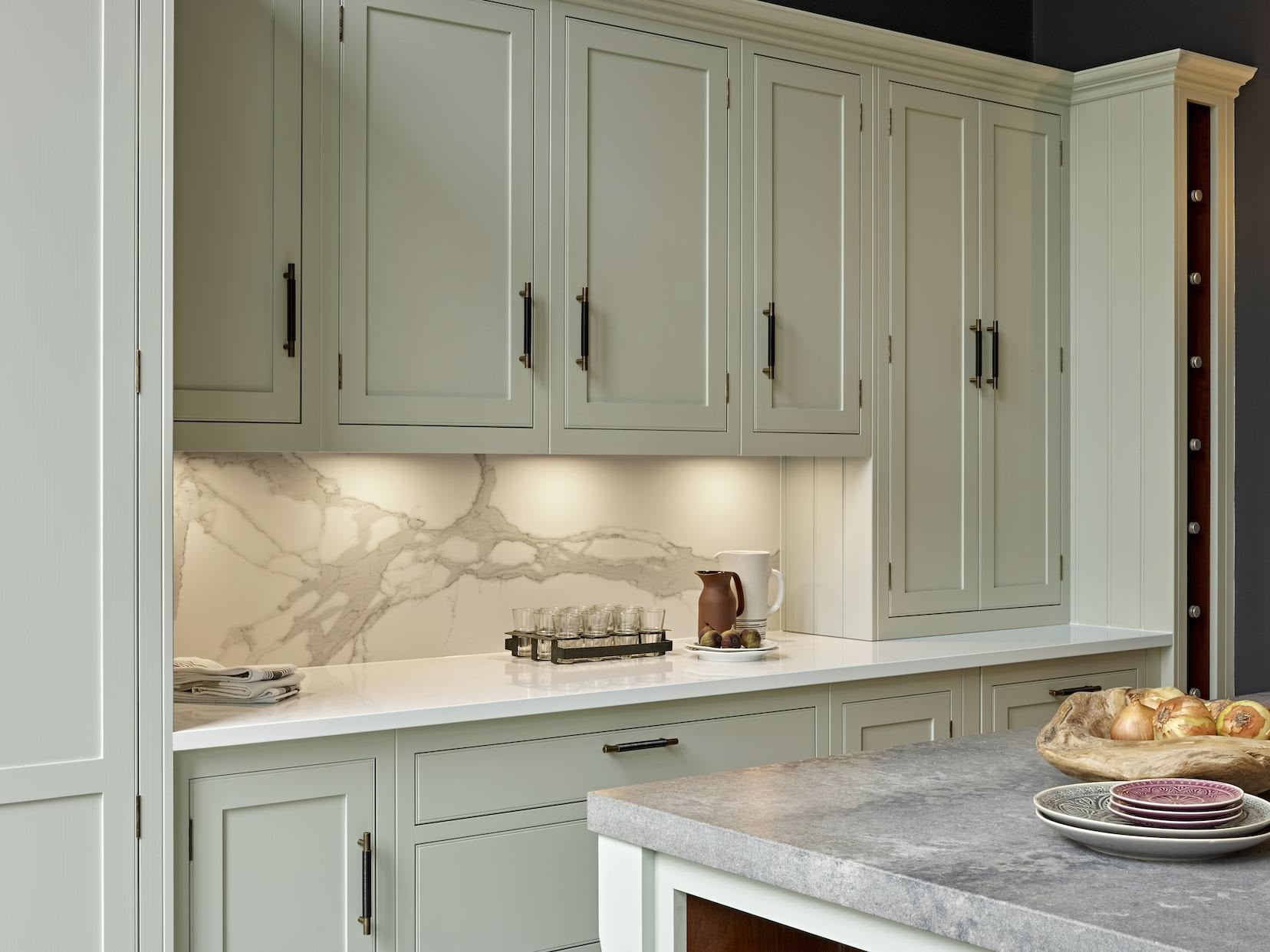 Pale green Arbor kitchen cabinetry with white work tops and kitchen island featuring a grey marble worktop
