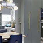 Green-grey kitchen cabinetry and gold handles with integrated oven next to open plan dining area