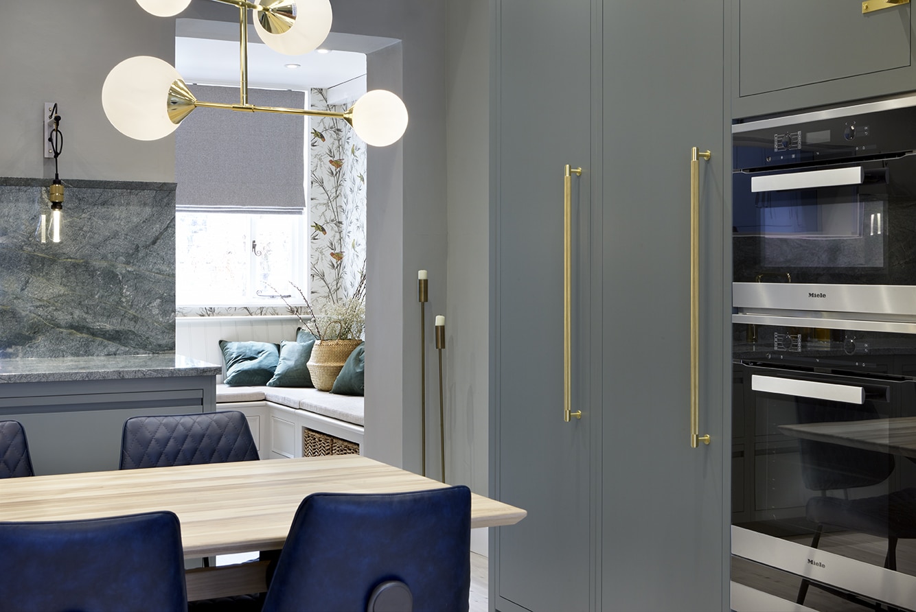 Green-grey kitchen cabinetry and gold handles with integrated oven next to open plan dining area