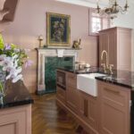Pink kitchen island with black marble worktop and white sink with gold tap