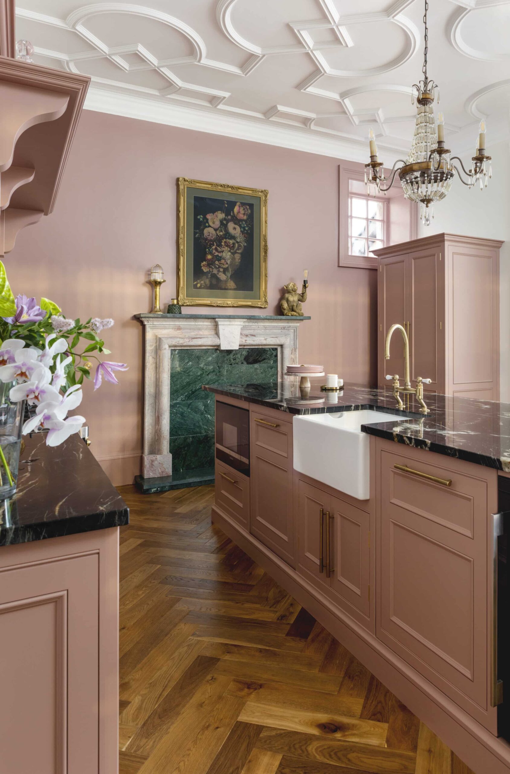 Pink kitchen island with black marble worktop and white sink with gold tap