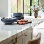 Closeup of a soft grey kitchen island with a white worktop and natural coloured stools