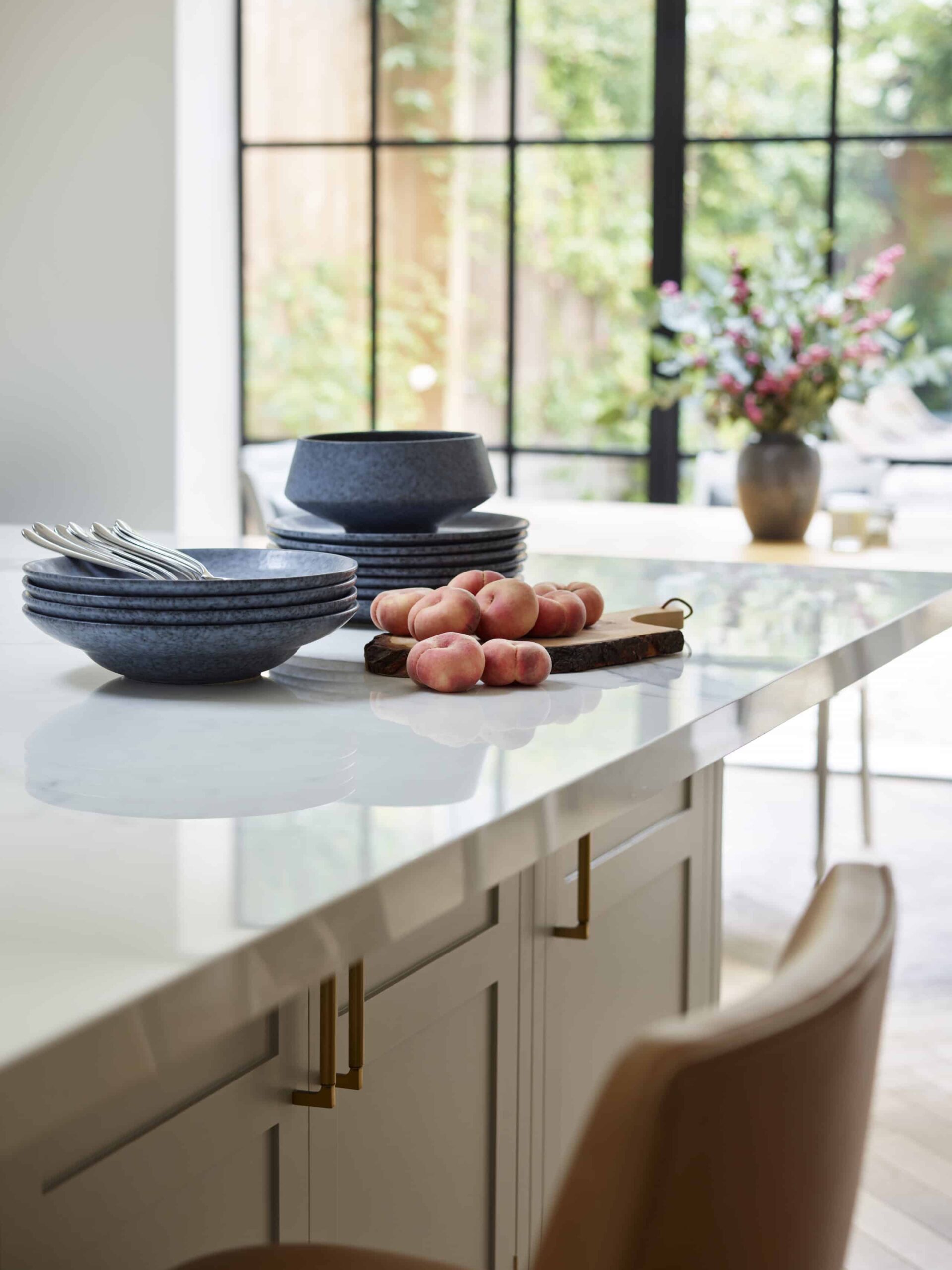 Closeup of a soft grey kitchen island with a white worktop and natural coloured stools