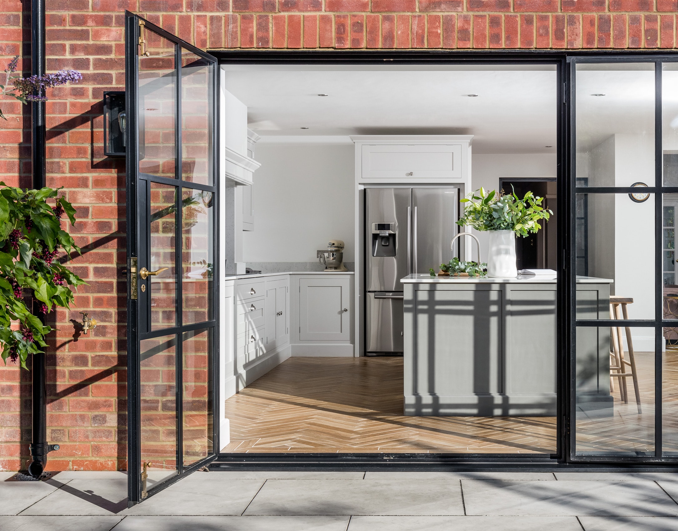 External view of bright Shaker kitchen seen through open glass slider doors