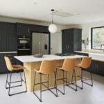 Light oak Shaker kitchen island with light grey worktop featuring orange stools overlooking dark Shaker kitchen cabinetry