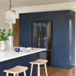 Deep blue kitchen island with white worktop in front of an American style refrigerator surrounded by Arbor cabinetry