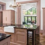 Pink kitchen island with black marble worktop and white sink with gold tap featuring wine fridge