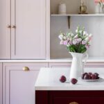 Closeup of Arbor kitchen cabinetry details in blush pink featuring gold handles with burgundy kitchen island with a white worktop