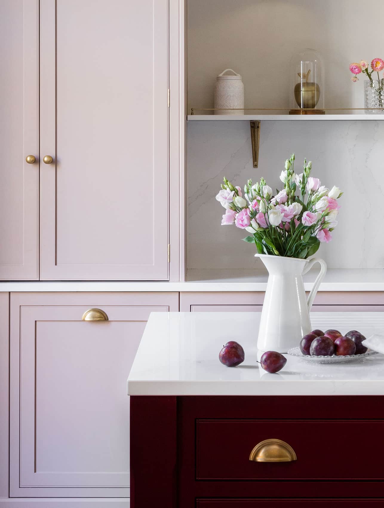 Closeup of Arbor kitchen cabinetry details in blush pink featuring gold handles with burgundy kitchen island with a white worktop