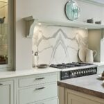 Pale green Arbor kitchen cabinetry with white worktops against a white and grey marble splashback behind the cooker