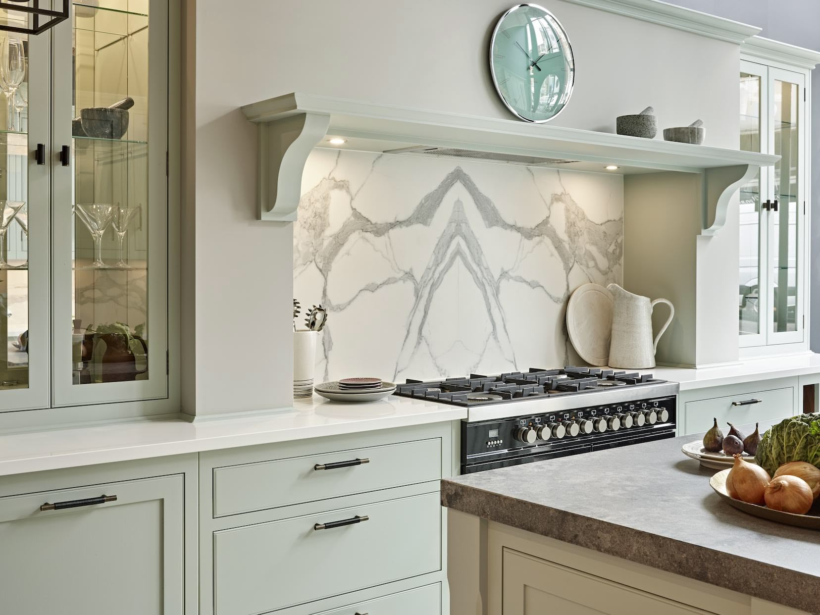 Pale green Arbor kitchen cabinetry with white worktops against a white and grey marble splashback behind the cooker