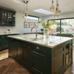 Vibrant green kitchen island with white worktop in front of open plan living area and large windows