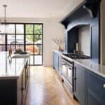 Rich blue kitchen cabinetry and cooker alcove featuring white worktops