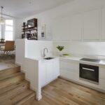 White linear Edge kitchen featuring natural wooden steps to open plan dining area