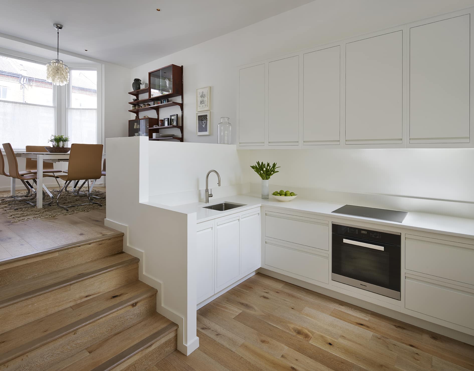 White linear Edge kitchen featuring natural wooden steps to open plan dining area
