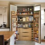 Green-grey tall kitchen pantry open to reveal walnut interior and organised storage