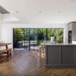 Deep grey Shaker kitchen island with natural wooden smile stools overlooking an open plan dining area