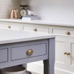 Closeup of blue kitchen island drawer with brass handle and walnut shelving