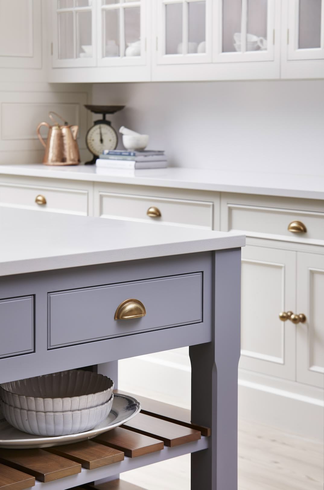 Closeup of blue kitchen island drawer with brass handle and walnut shelving
