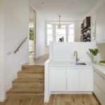 White linear Edge kitchen featuring natural wooden steps to open plan dining area