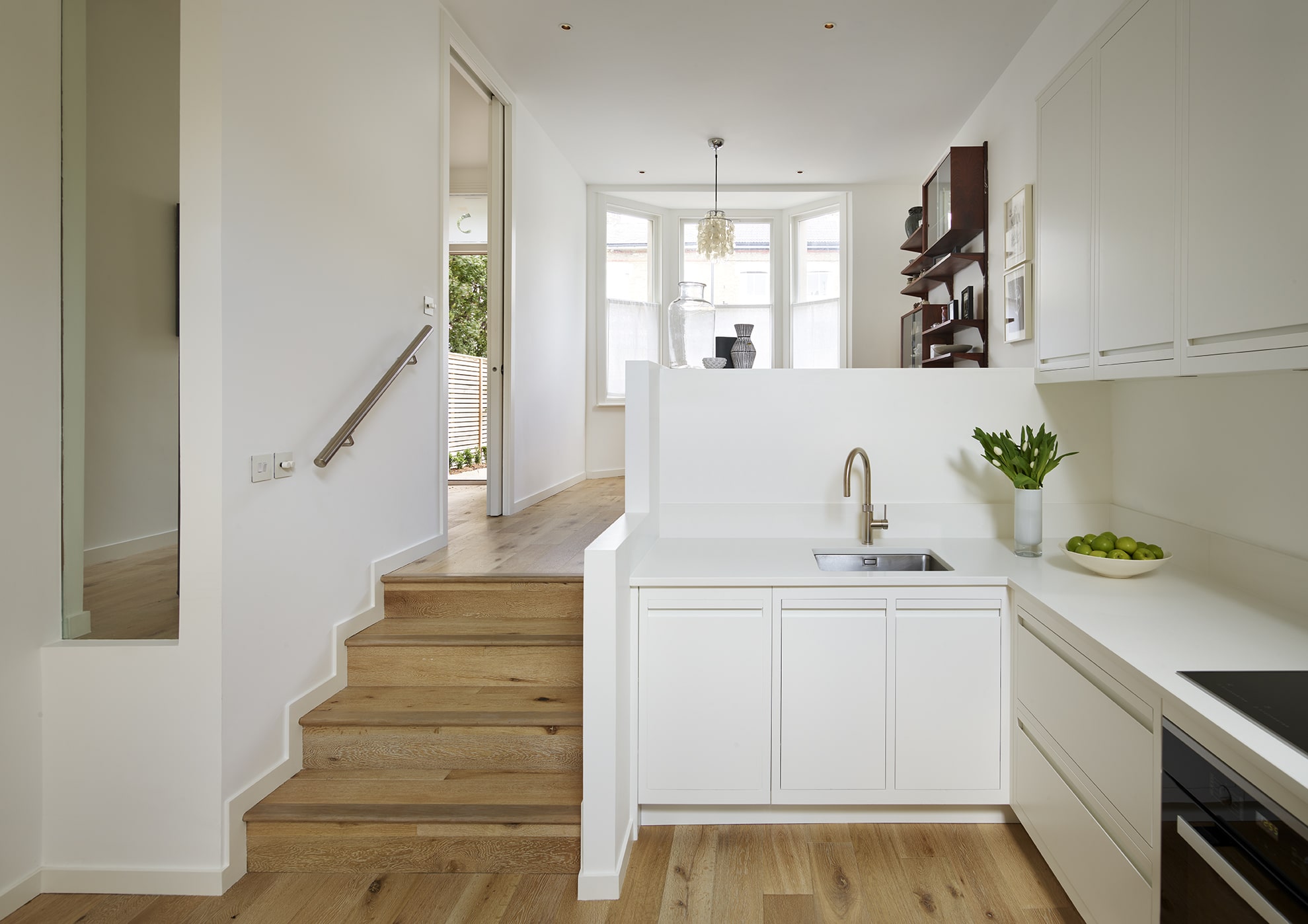 White linear Edge kitchen featuring natural wooden steps to open plan dining area