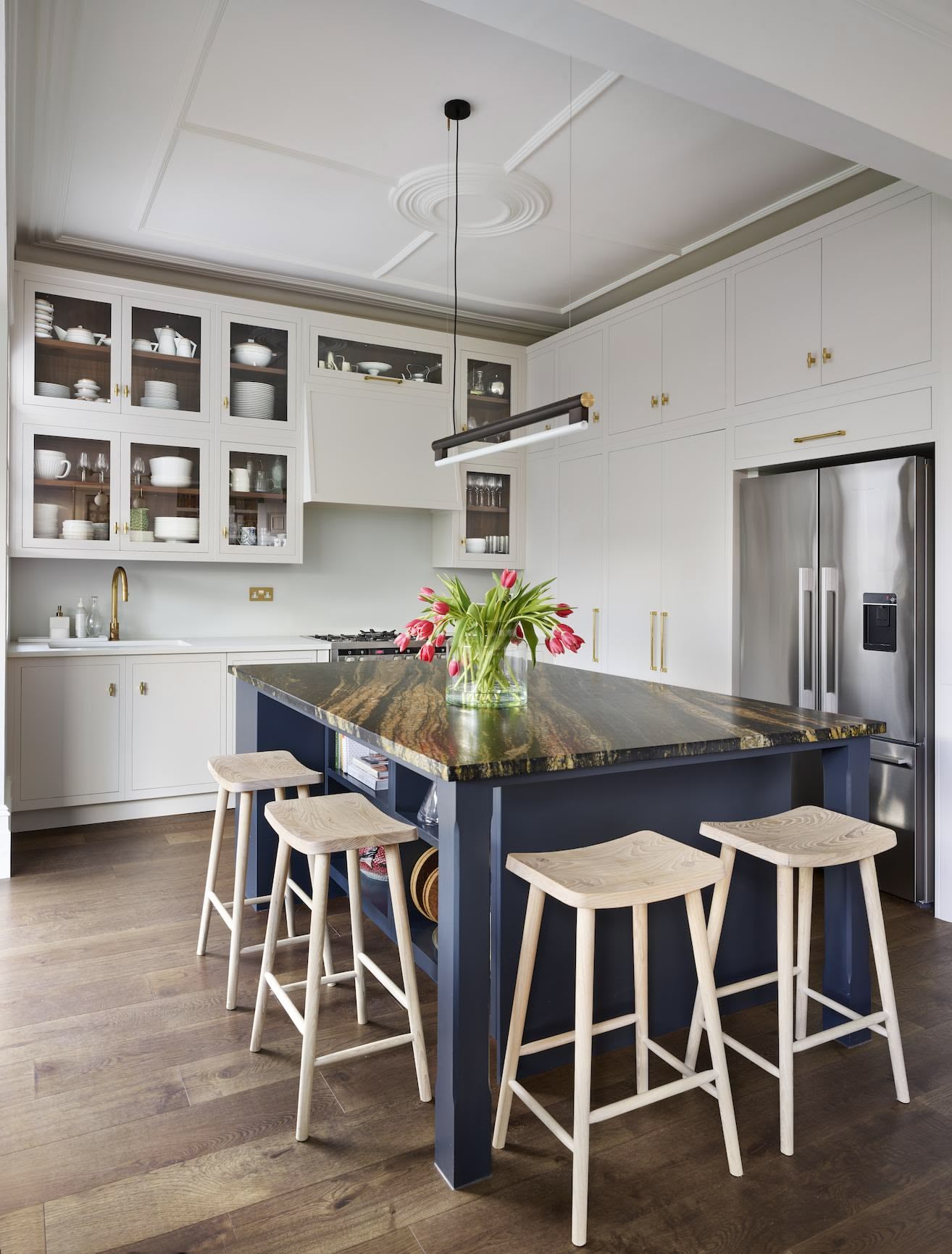 Blue kitchen island with black and brown marble worktop and natural wooden smile stools