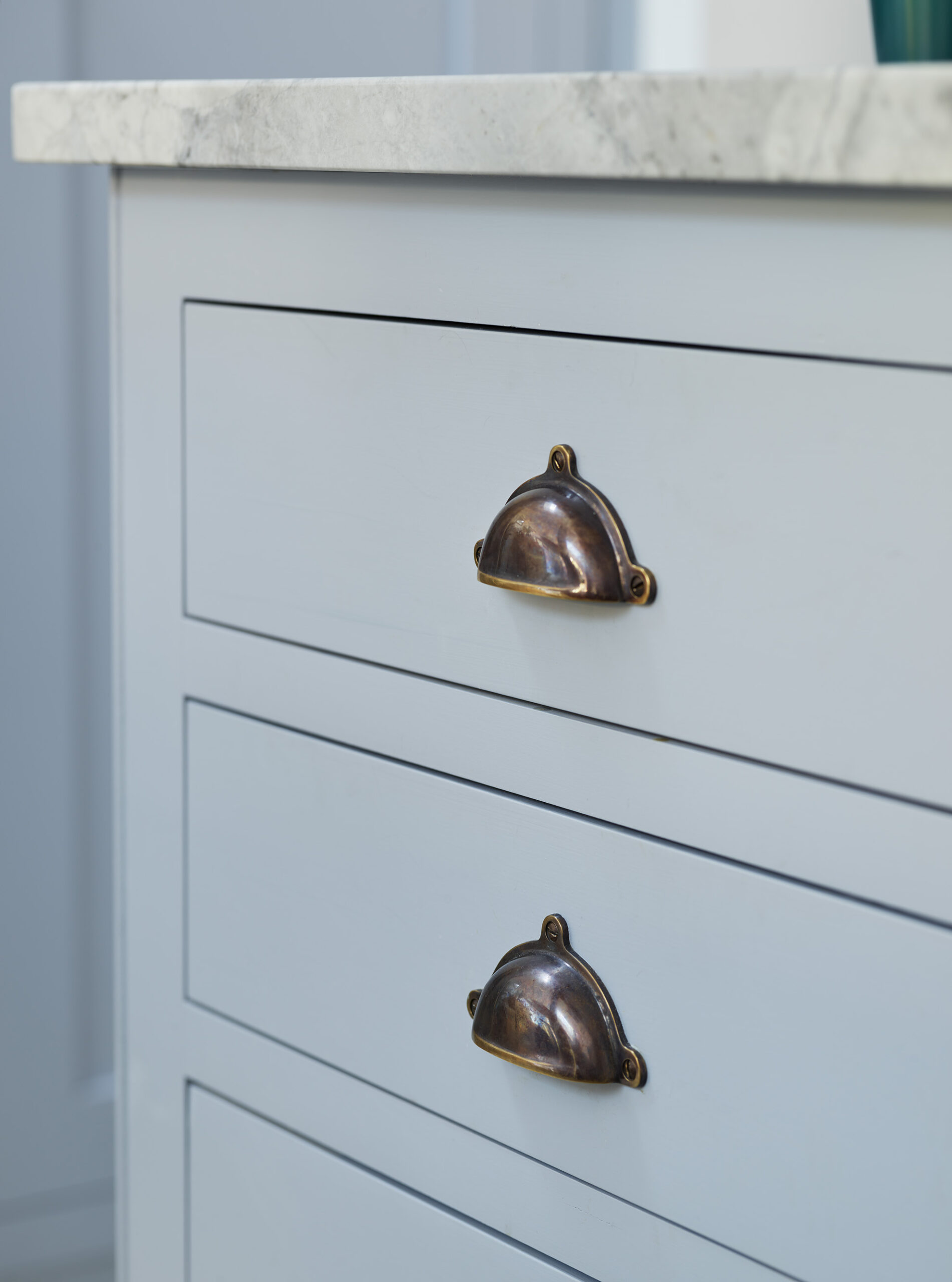 Closeup of pale blue Shaker drawers with antique brass handles