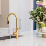 Closeup of white kitchen worktop with silver integrated sink and gold tap