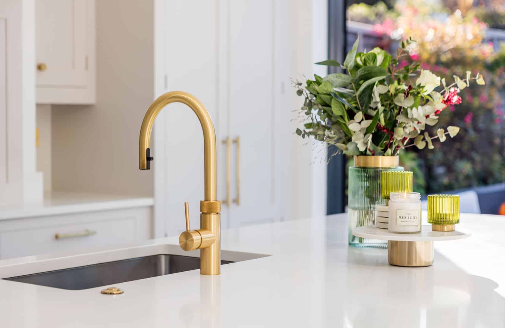 Closeup of white kitchen worktop with silver integrated sink and gold tap