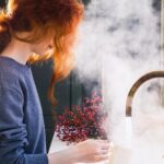 Woman using brass tap in front of deep green Shaker kitchen cabinetry