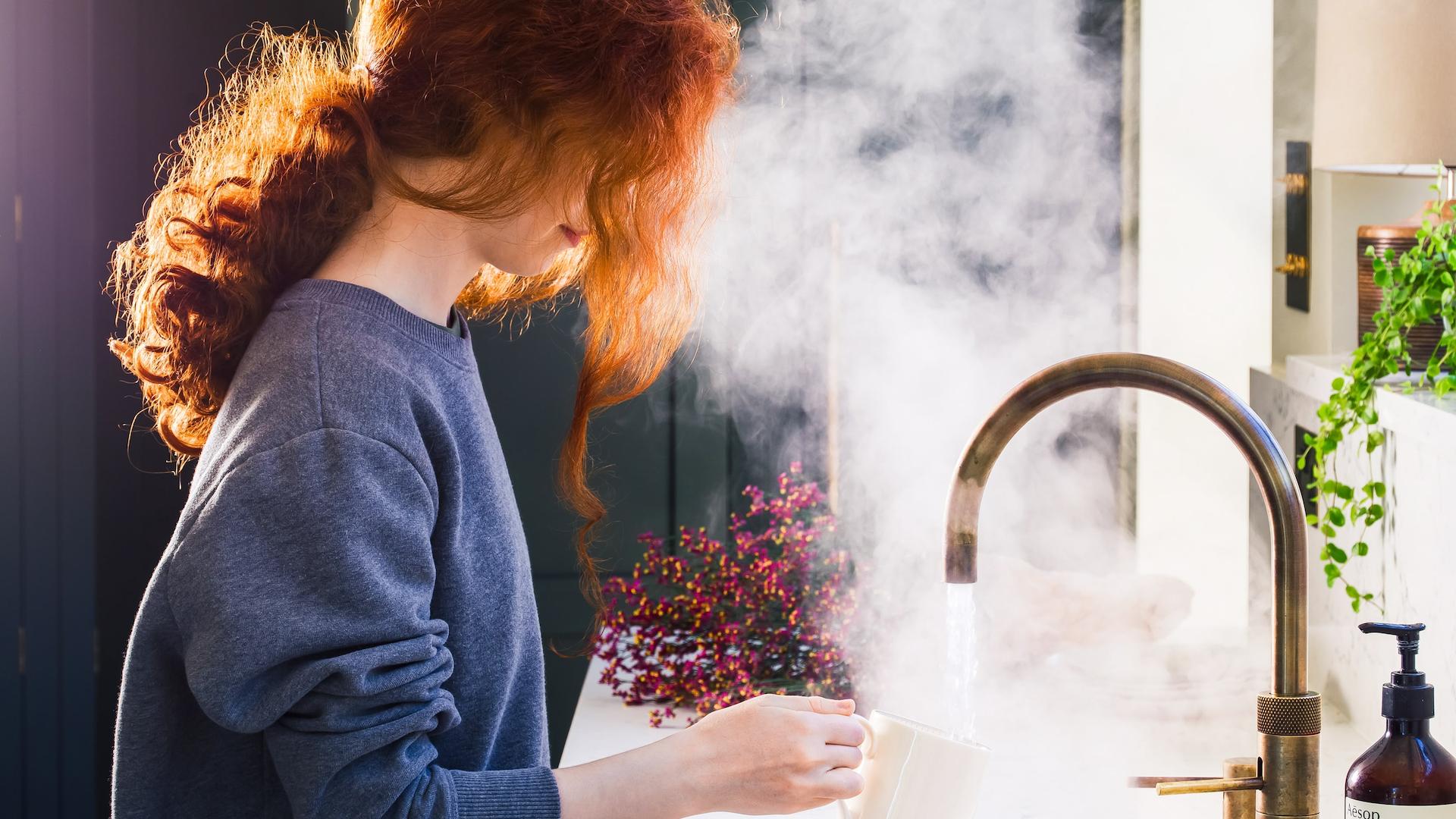 Woman using brass tap in front of deep green Shaker kitchen cabinetry