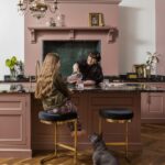 Mother and young daughter around pink kitchen island with black worktop featuring gold and black stools