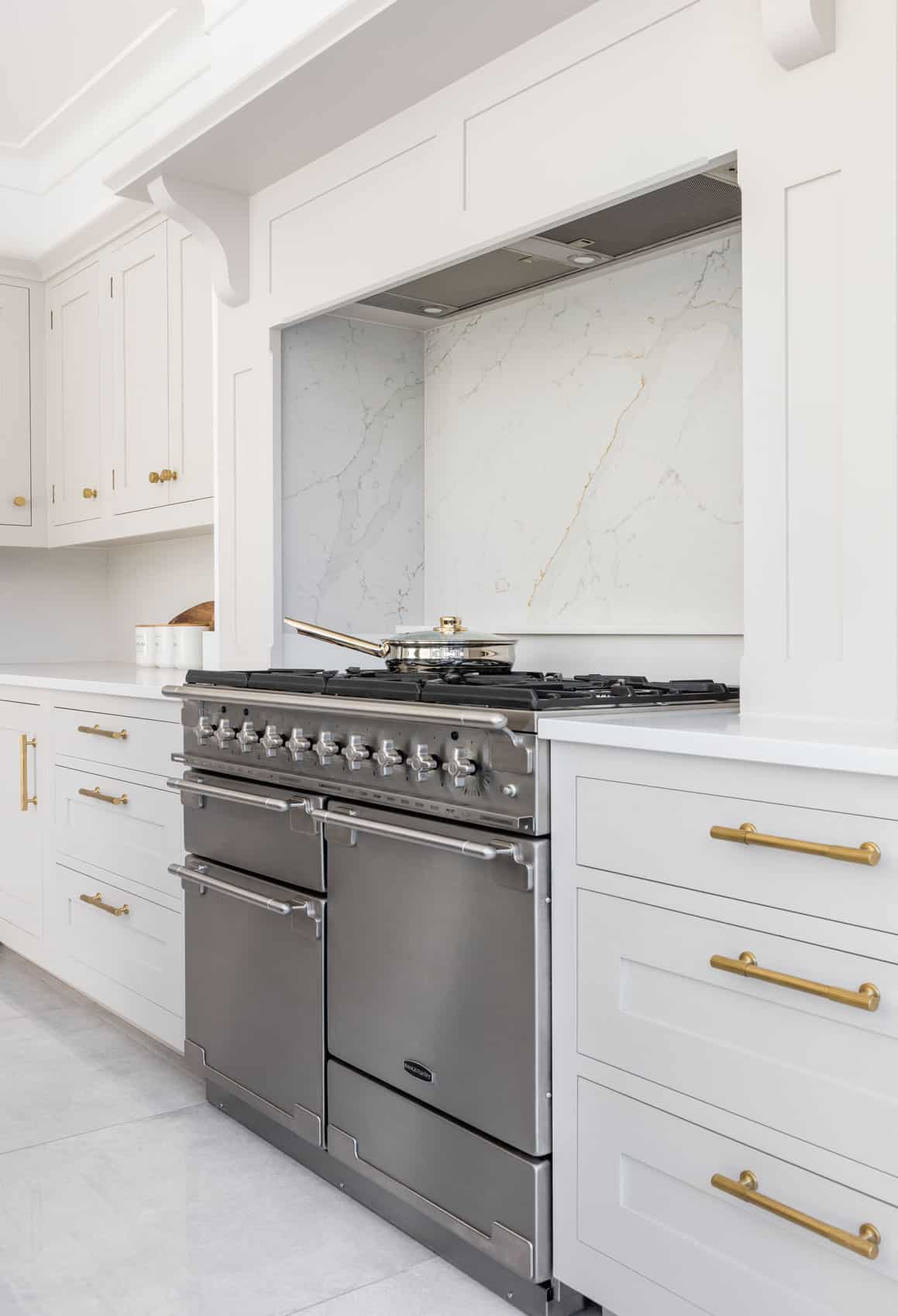 Cooker surrounded by white Shaker kitchen cabinetry with white marble splashback