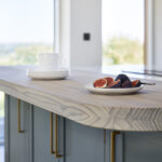 Closeup of a blue kitchen island featuring Arbor cabinetry with gold handles and a natural wood worktop