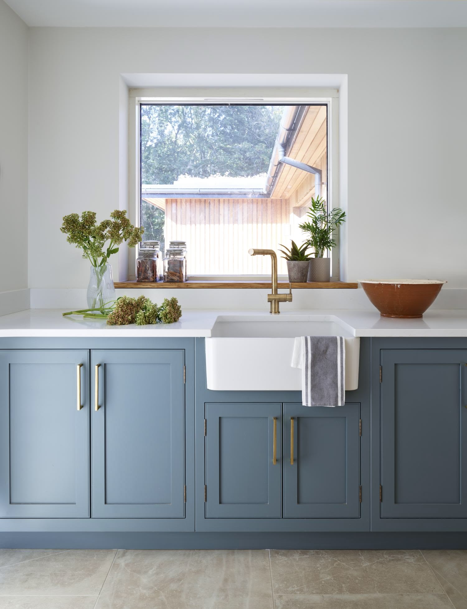 Blue utility room cabinetry with white worktop featuring white basin sink with gold tap