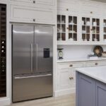 White kitchen cabinetry with wine rack alongside American style fridge
