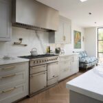 Soft grey kitchen cabinetry with white worktops and white and grey marble splashback against the cooker