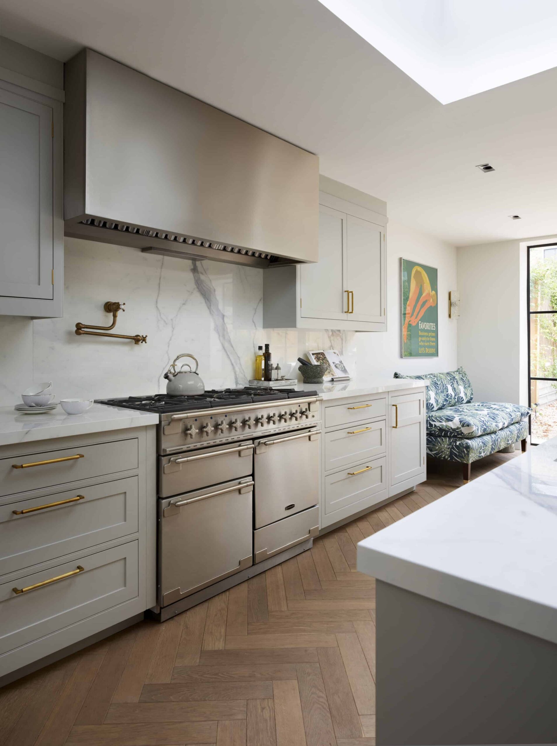 Soft grey kitchen cabinetry with white worktops and white and grey marble splashback against the cooker